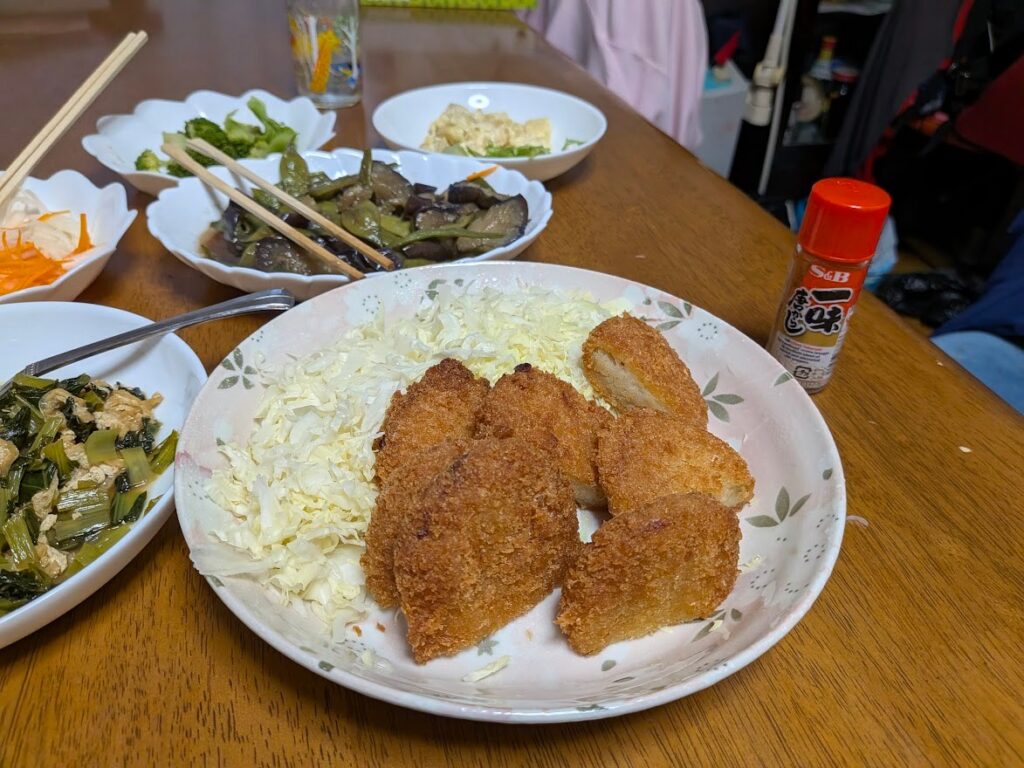 コロッケとキャベツ、青菜と油揚げ、ナスとピーマンの炒め物など。夕食の大皿は夫婦二人分